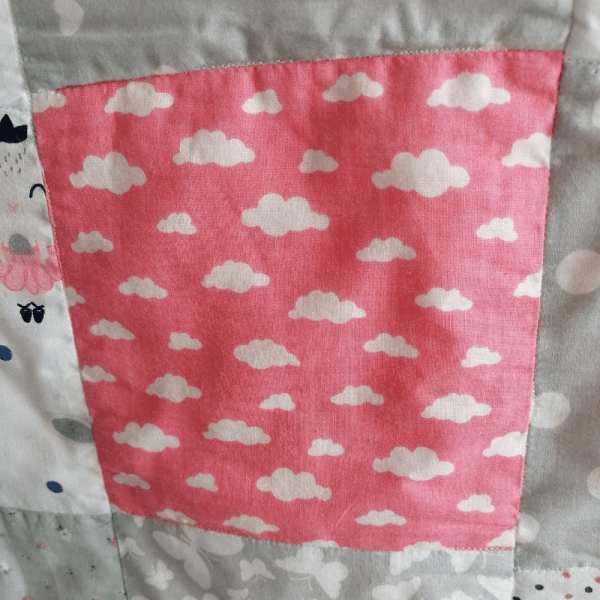 skiautinių antklodės fragmentas su debesėliais rožiniame fone